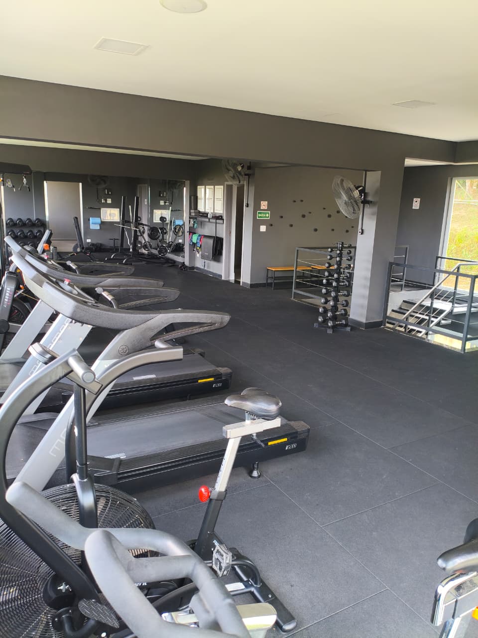 Academia equipada com esteiras, bike e área de musculação iluminada por luz natural