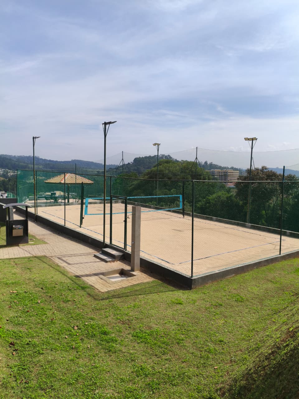 Quadra de beach tênis com areia, rede azul e vista panorâmica para o vale
