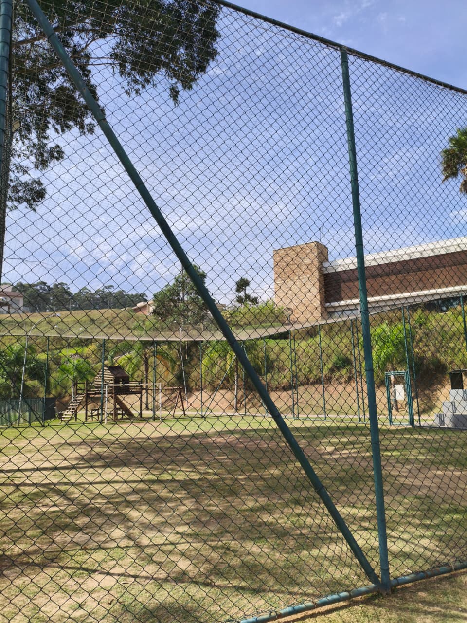 Campinho visto de fora do alambrado com playground e Salão de Festas ao fundo
