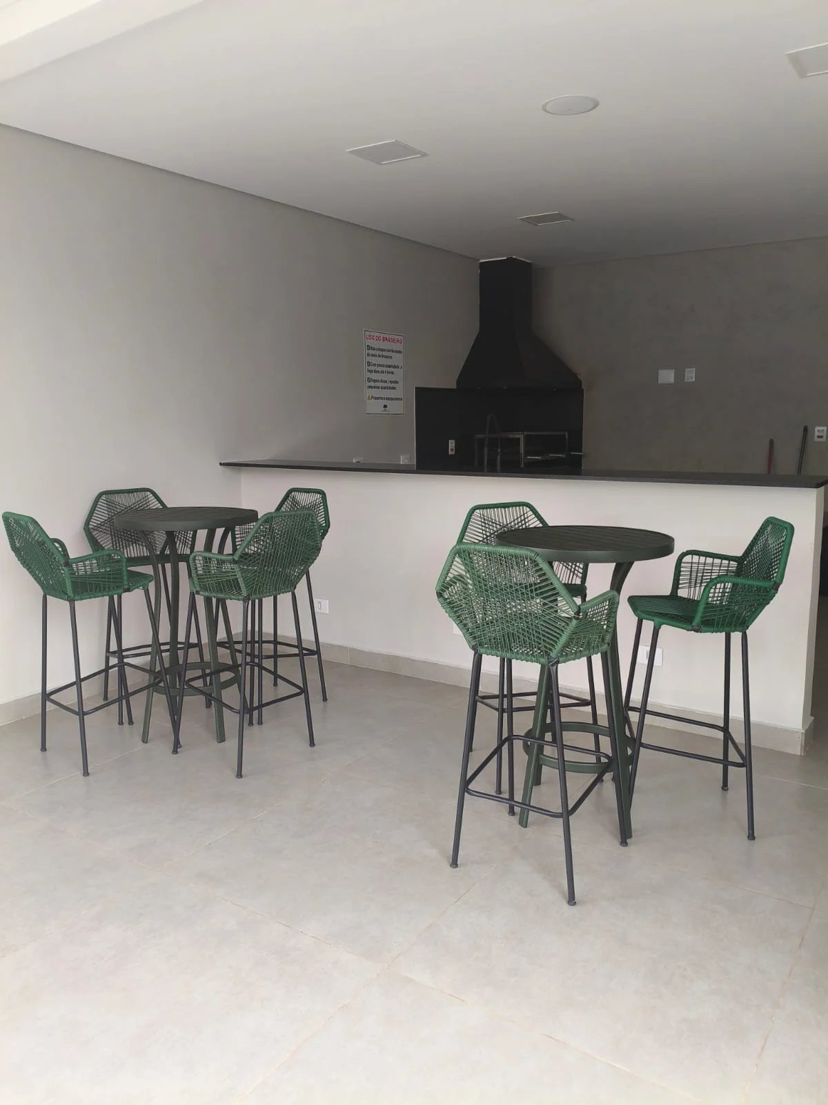 Espaço gourmet com churrasqueira, mesas altas e banquetas verdes para confraternizações
