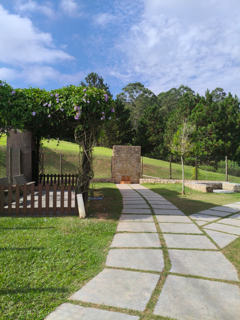 Pergolado florido com flores lilás e caminho de pedras no Espaço Pet do Campos do Conde