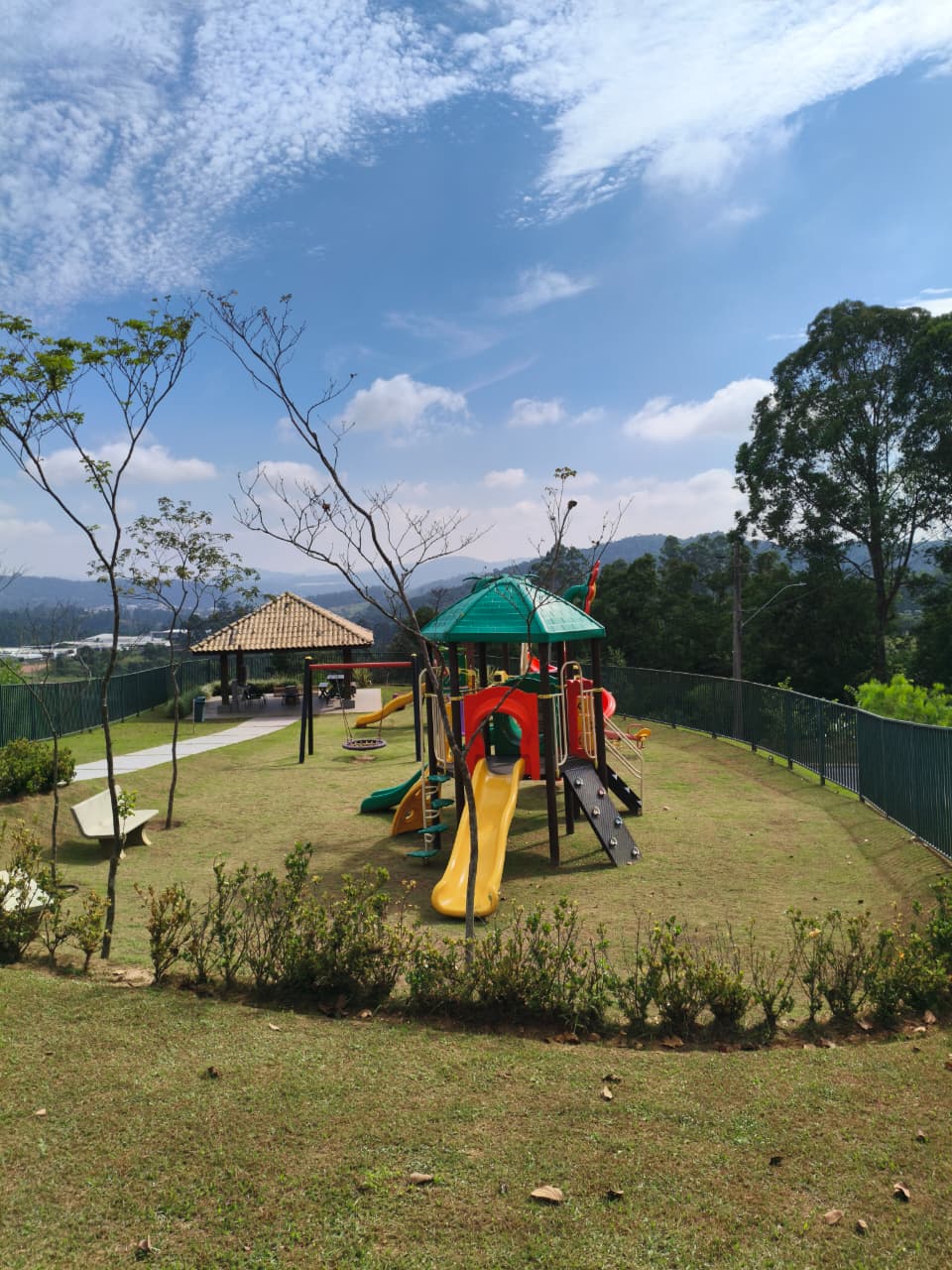 Parquinho infantil colorido com escorregador, balanço e quiosque, com vista panorâmica para as montanhas